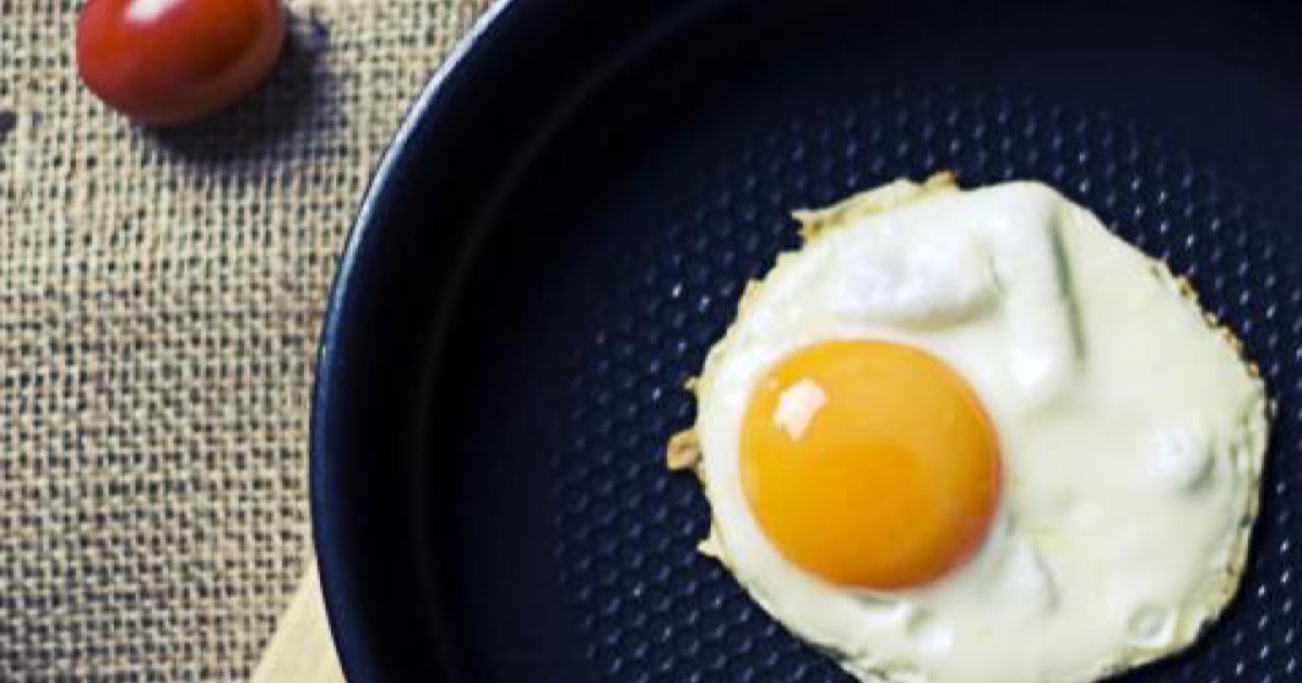 A fried egg in a dark skillet next to a tomato on a woven mat.