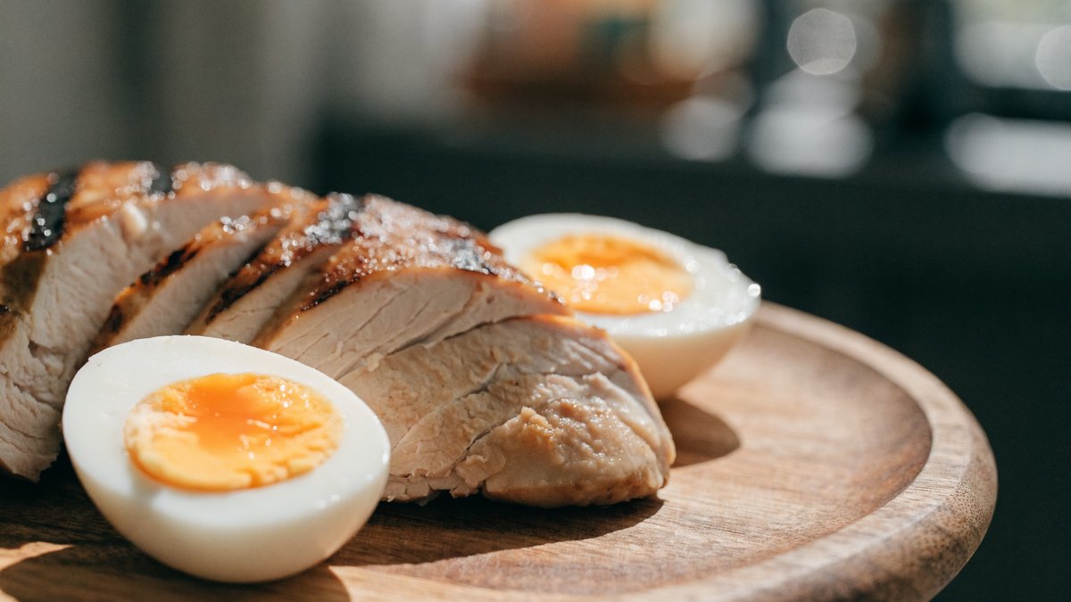 Sliced grilled chicken breast and boiled eggs on a wooden board