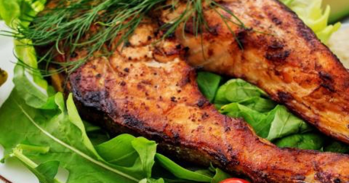 Two grilled salmon steaks resting on a bed of arugula and spinach with dill and a lime wedge.
